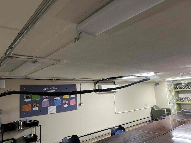 Responded to service call for fallen mini split refrigerant piping on 2024 equipment. Upon arrival, found refrigerant line set and associated conduit had detached from ceiling mounting points in what appears to be a classroom or commercial space. Secured and re-supported the refrigerant piping and electrical conduit using proper metal clamps and straps along the ceiling run to the indoor wall-mounted evaporator unit. Verified system operation and ensured all line sets were properly supported to prevent future sagging or detachment.