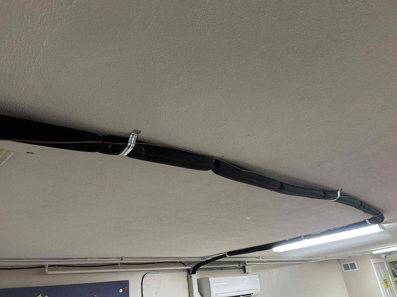 Responded to service call for fallen mini split refrigerant piping on 2024 equipment. Upon arrival, found refrigerant line set and associated conduit had detached from ceiling mounting points in what appears to be a classroom or commercial space. Secured and re-supported the refrigerant piping and electrical conduit using proper metal clamps and straps along the ceiling run to the indoor wall-mounted evaporator unit. Verified system operation and ensured all line sets were properly supported to prevent future sagging or detachment.