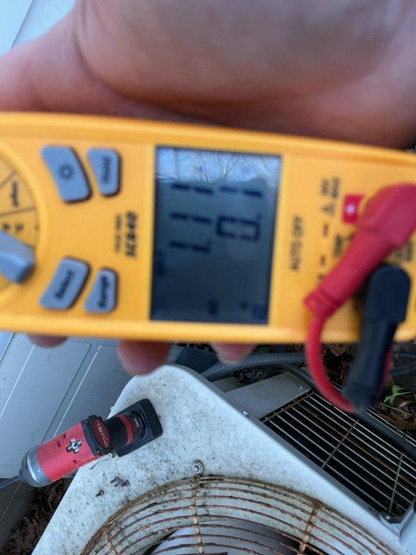 Completed annual preventative maintenance on residential air conditioning condenser unit. Performed comprehensive system inspection including electrical testing with multimeter showing proper voltage readings at 12.3V, verified fan motor operation and inspected protective grille showing normal weathering. Cleared accumulated debris and leaves from around unit and decking area to ensure proper airflow and drainage. All components operating within normal parameters upon completion.