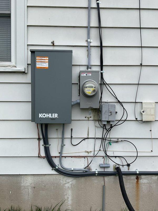 Completed installation of a 10kW residential standby generator with integrated Kohler transfer switch and new 100-amp electrical panel. Mounted transfer switch and metering equipment on exterior wall with proper conduit routing and weather-tight connections. Installed gas supply line with shutoff valve and connected to existing natural gas system. All electrical components secured to building exterior with appropriate hardware, conduit straps, and junction boxes per code requirements. System tested and operational upon completion.