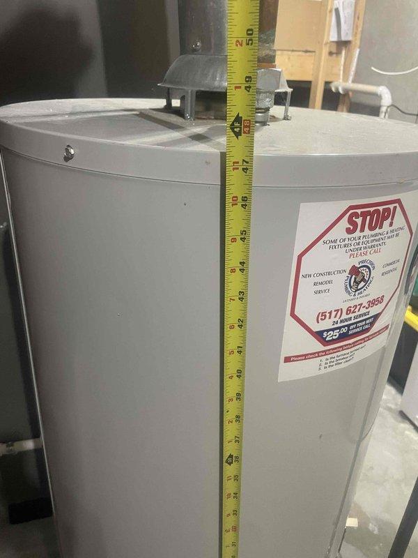 Responded to service call for leaking water heater in residential basement. Upon inspection, confirmed active leak from original water heater installed in 2007, indicating unit has reached end of serviceable life after approximately 18 years of operation. Documented existing equipment specifications and measurements, noting standard cylindrical tank configuration with overhead black metal flue pipe connection and brass drain valve at base. Assessed surrounding mechanical room infrastructure including proximity to HVAC system, electrical panel, and existing plumbing connections. Photographed current installation setup showing water heater positioning relative to concrete walls, overhead ductwork, and utility access points. Measured tank dimensions to determine replacement specifications and clearance requirements for new unit installation. Evaluated venting configuration and gas line connections to ensure compliance with current code requirements for replacement equipment. Prepared comp