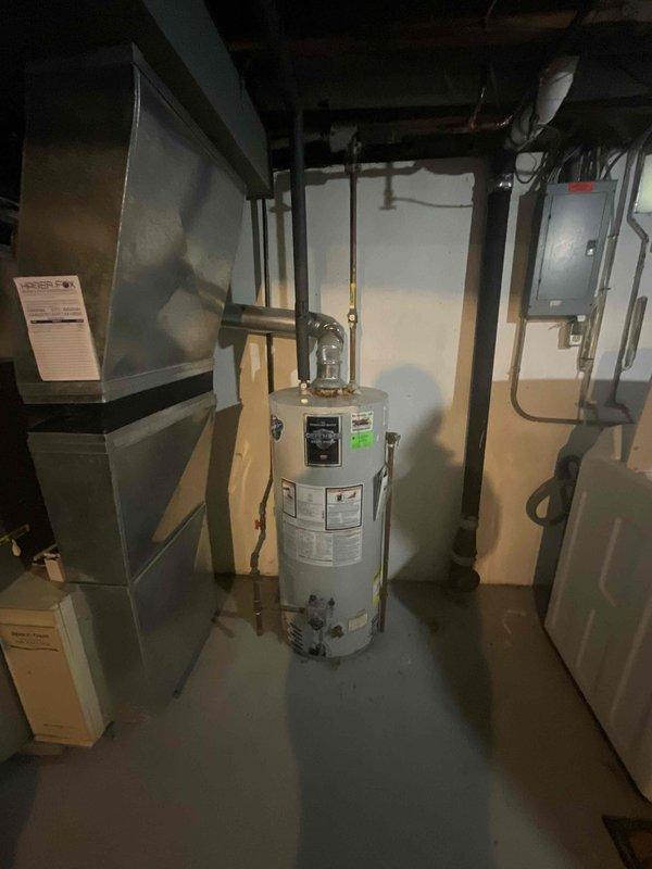 Conducted on-site assessment of non-functional natural draft water heater in basement utility room. Evaluated existing standard tank-type water heater with natural draft venting system and documented tight piping configuration that prevented accurate phone estimate. Photographed current installation including copper supply lines, venting arrangement, and spatial constraints to prepare detailed replacement estimate for standard water heater unit.