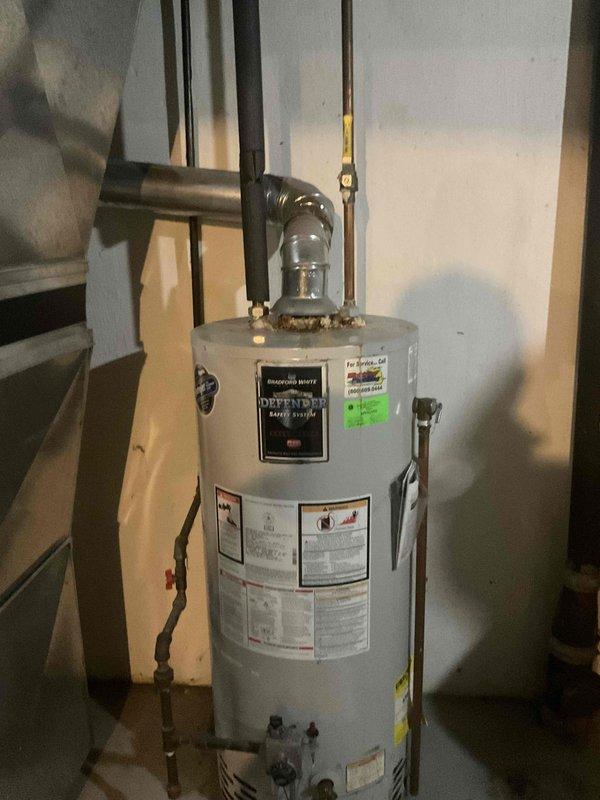 Conducted on-site assessment of non-functional natural draft water heater in basement utility room. Evaluated existing standard tank-type water heater with natural draft venting system and documented tight piping configuration that prevented accurate phone estimate. Photographed current installation including copper supply lines, venting arrangement, and spatial constraints to prepare detailed replacement estimate for standard water heater unit.