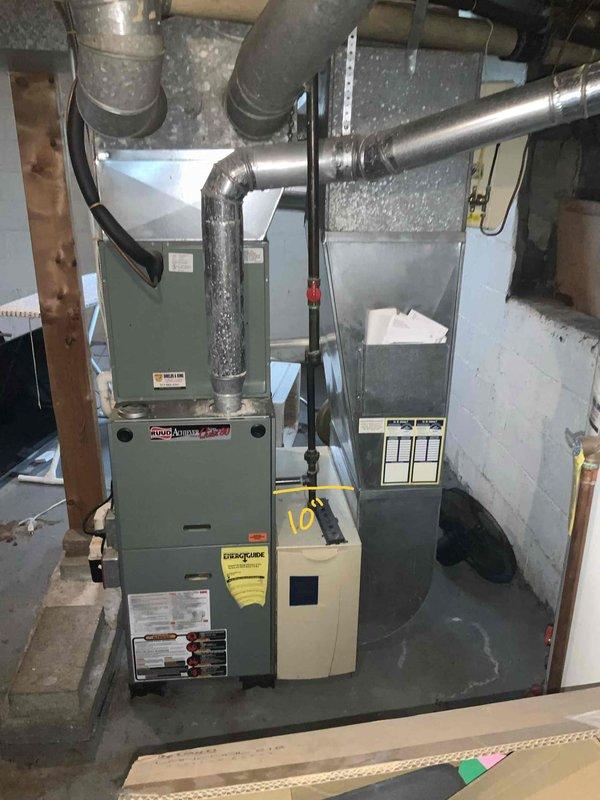 Performed estimate for replacement of 20-year-old furnace system in residential basement mechanical room. Assessed existing greenish-gray furnace unit with connected galvanized ductwork, humidifier accessory, and air handler components showing age-related wear and debris accumulation. Documented current HVAC configuration including horizontal duct runs, concrete utility space layout, and auxiliary equipment to provide comprehensive replacement quote and present available promotional offerings for comparison with other contractors.