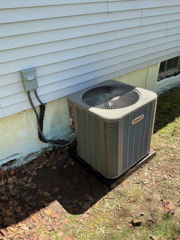 Completed installation of 2.5-ton Lennox air conditioning system with matching evaporator coil on left side of residential property. Unit positioned on composite pad against exterior wall with proper clearances, electrical disconnect box mounted to siding, and refrigerant lines connected. System commissioned and tested for proper operation, with all electrical connections completed per code requirements.