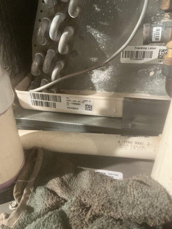 Completed comprehensive air conditioning maintenance service on residential HVAC system, focusing on evaporator coil assembly and air handler unit. Performed thorough inspection of A-frame evaporator coil configuration, verified proper refrigerant line connections at brass fittings, and confirmed condensate drain system operation through white PVC piping. Cleaned coil fins, checked serpentine refrigerant tubing for proper flow, and inspected metallic conduit connections. Documented equipment condition with detailed photography showing unit labels, tracking information, and component specifications. System operational and ready for cooling season.