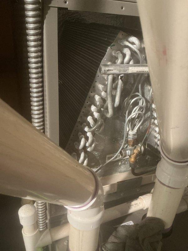 Completed comprehensive air conditioning maintenance service on residential HVAC system, focusing on evaporator coil assembly and air handler unit. Performed thorough inspection of A-frame evaporator coil configuration, verified proper refrigerant line connections at brass fittings, and confirmed condensate drain system operation through white PVC piping. Cleaned coil fins, checked serpentine refrigerant tubing for proper flow, and inspected metallic conduit connections. Documented equipment condition with detailed photography showing unit labels, tracking information, and component specifications. System operational and ready for cooling season.