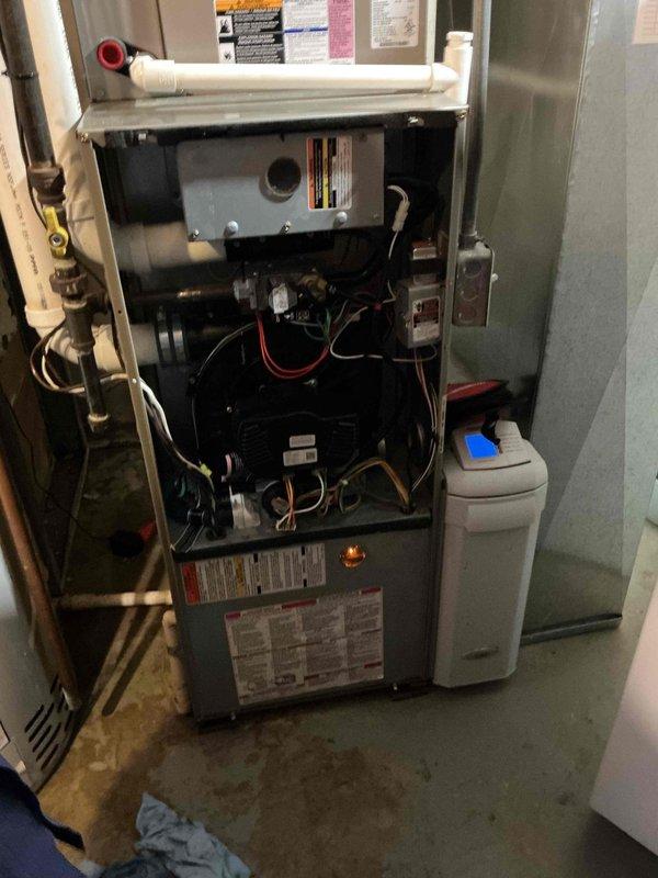 Responded to service call for water leak of unknown origin in residential HVAC system. Upon arrival, performed visual inspection of furnace, air handler, water heater, and associated plumbing connections in basement utility area. Examined condensate drain lines, PVC piping, copper water lines, and all visible connections for signs of active leaking or moisture accumulation. Inspected furnace cabinet interior components, blower assembly, and drain pan for water presence. Checked water heater connections and relief valve for potential leak sources. Documented equipment conditions with photos showing furnace with open access panel, internal components, condensate piping, water softener system, air handler unit, and water heater installation. No active leak identified during inspection period. Advised monitoring system for recurrence and recommended callback if leak reappears for further diagnostic evaluation.