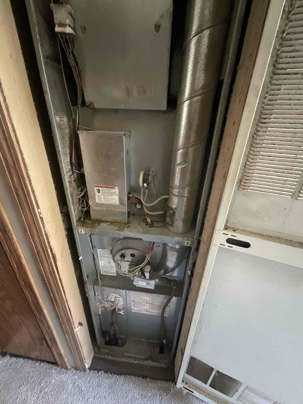 Conducted comprehensive evaluation of existing HVAC system for full replacement estimate. Assessed 33-year-old Amana air conditioning condenser unit located on exterior concrete pad and corresponding indoor air handler/furnace equipment housed in confined utility closet. Both heating and cooling components have reached end of useful service life, showing significant age-related wear and obsolescence. Documented current equipment configuration including refrigerant line routing, electrical connections, ductwork arrangement, and spatial constraints within mechanical closet. Photographed outdoor condenser positioning against building siding and indoor vertical equipment installation to determine replacement specifications and identify any installation challenges. Evaluated adequate clearances, existing concrete pad condition, and access requirements for future equipment removal and installation.