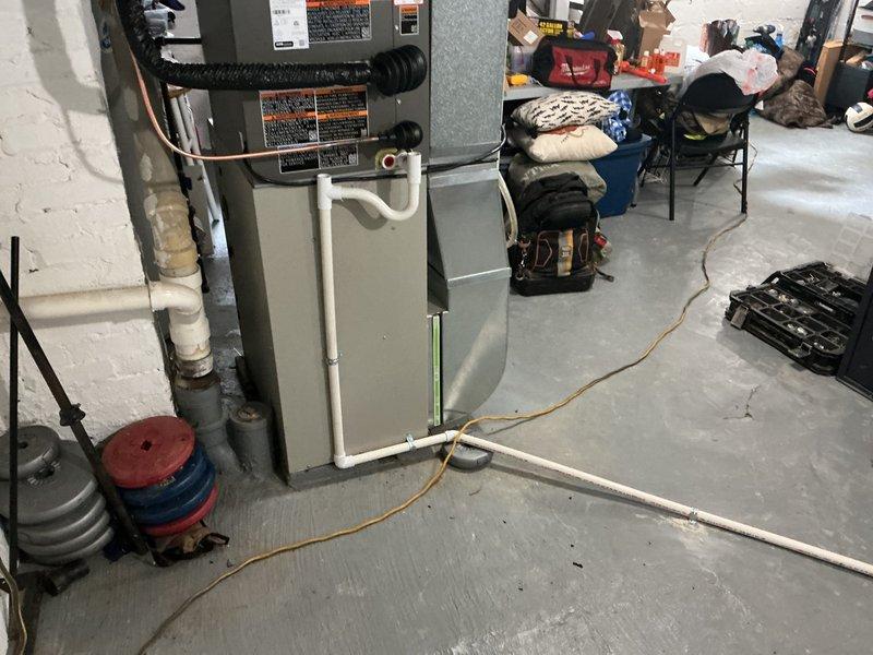 Successfully completed installation of 2-ton air conditioning unit with matching evaporator coil in residential basement location. Reconnected rear-mounted condenser unit to existing ductwork and established proper refrigerant lines and drainage system using white PVC piping. All mechanical connections secured to furnace/air handler, system tested and verified operational per manufacturer specifications.