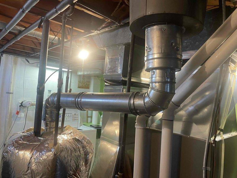 Conducted on-site evaluation of existing water heater system for replacement estimate. Assessed current unit configuration including insulated tank, pipe connections, venting arrangement, and clearance requirements in mechanical room. Documented equipment specifications, installation conditions, and spatial constraints to develop comprehensive replacement proposal. Photographed existing water heater with reflective insulation wrap, black supply/discharge pipes, and proximity to HVAC equipment to ensure accurate sizing and compatibility recommendations for new unit installation.