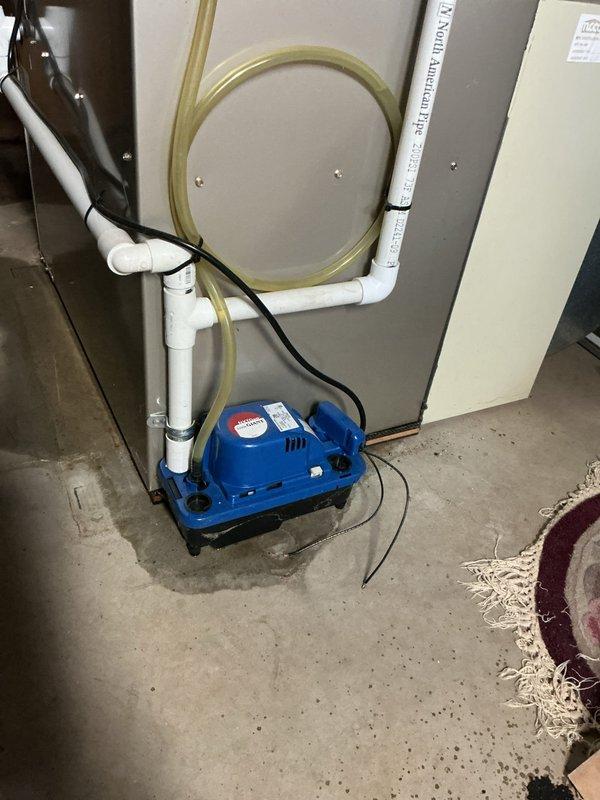 Responded to service call for leaking condensate pump on 2014 HVAC system located in basement. Upon arrival, found significant water staining and moisture accumulation on concrete floor surrounding condensate pump unit, indicating active leak. Inspected blue/white condensate pump assembly with black reservoir base and associated PVC discharge piping. Identified source of leak and performed necessary repairs to pump connections and drainage system. Verified proper pump operation, confirmed all tubing and pipe connections were secure, and tested discharge flow. System restored to normal operation with no further leakage observed at time of departure.