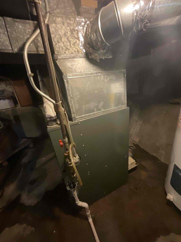 Completed estimate for replacement of 23-24 year old furnace unit located in basement utility area. Assessed existing green metal furnace cabinet with connected gas lines, refrigerant piping with insulation wrap, and metallic ductwork including flexible ducting connections. Provided estimate options for furnace replacement and new air conditioning system installation, as property currently has no AC equipment. Evaluated exterior electrical service panel and conduit routing on home's exterior wall for potential AC unit power requirements and equipment placement considerations.