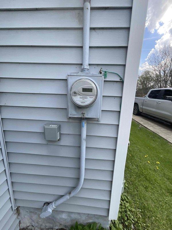 Completed estimate for replacement of 23-24 year old furnace unit located in basement utility area. Assessed existing green metal furnace cabinet with connected gas lines, refrigerant piping with insulation wrap, and metallic ductwork including flexible ducting connections. Provided estimate options for furnace replacement and new air conditioning system installation, as property currently has no AC equipment. Evaluated exterior electrical service panel and conduit routing on home's exterior wall for potential AC unit power requirements and equipment placement considerations.