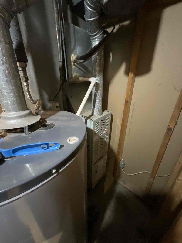 Performed comprehensive assessment of existing 16-20 year old HVAC system with non-functional AC condenser compressor due to age-related deterioration and weather corrosion. Inspected outdoor condensing unit with cylindrical configuration, noting advanced wear on compressor components and external housing. Evaluated indoor furnace and air handler equipment located in basement utility area, examining ductwork connections, gas line installations, and electrical service. Documented complete system configuration including water heater proximity, PVC condensate drainage, flexible gas connections, and electrical disconnect box placement at exterior wall. Provided comprehensive estimate options for full system replacement including new furnace and AC condenser unit, as well as alternative pricing for condenser-only replacement to meet immediate seasonal cooling needs.