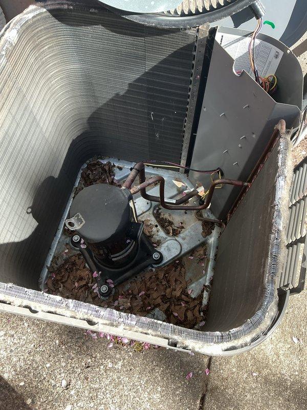 Performed scheduled maintenance on residential air conditioning system. Inspected indoor evaporator coil assembly, noting dust accumulation on serpentine copper tubing and heat exchanger surfaces. Examined outdoor condensing unit, removing top panel to access internal components including condenser coil, compressor, and electrical controls. Cleared significant debris accumulation of dried leaves and organic matter from unit base and compartment areas around compressor. Verified refrigerant line connections, brass fittings, and electrical wiring at both indoor and outdoor units. System components operational upon completion of maintenance service.