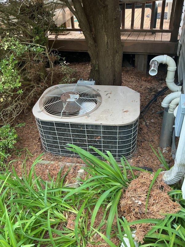 Completed annual preventive maintenance on residential outdoor condensing unit located beneath elevated deck structure. Performed comprehensive inspection of cylindrical unit including fan motor operation, electrical connections, refrigerant pressures, and condenser coil condition. Cleaned debris from top cover and verified proper airflow through wire mesh grille and fan assembly. Inspected PVC condensate drain line for proper operation and drainage. Unit operating within normal parameters upon completion of scheduled maintenance service.
