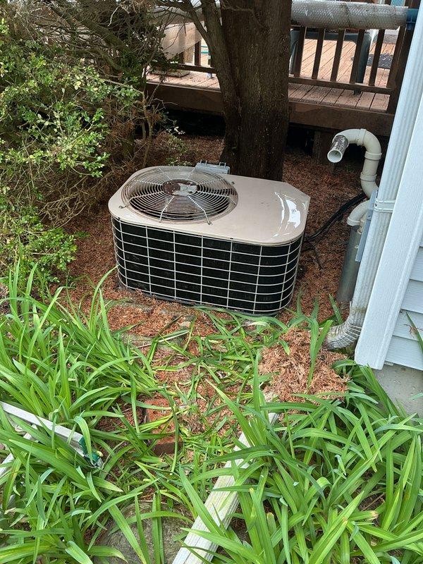 Completed annual preventive maintenance on residential outdoor condensing unit located beneath elevated deck structure. Performed comprehensive inspection of cylindrical unit including fan motor operation, electrical connections, refrigerant pressures, and condenser coil condition. Cleaned debris from top cover and verified proper airflow through wire mesh grille and fan assembly. Inspected PVC condensate drain line for proper operation and drainage. Unit operating within normal parameters upon completion of scheduled maintenance service.