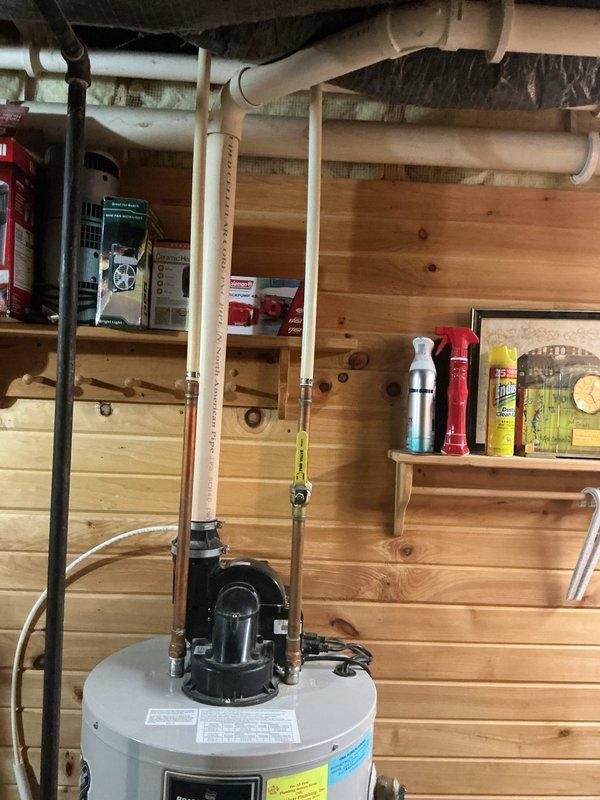 Responded to service call for reported water leak at base of standard tank water heater. Upon arrival, conducted thorough inspection of unit and surrounding plumbing connections. Examined tank integrity, temperature and pressure relief valve, drain valve, and all inlet/outlet connections for signs of active leakage or moisture accumulation. Inspected copper supply lines and PVC discharge piping for proper installation and secure mounting. Verified pump assembly operation and checked all connection points for potential leak sources. Documented existing conditions with photography showing water heater installation, piping configuration, and utility room setup for service records.