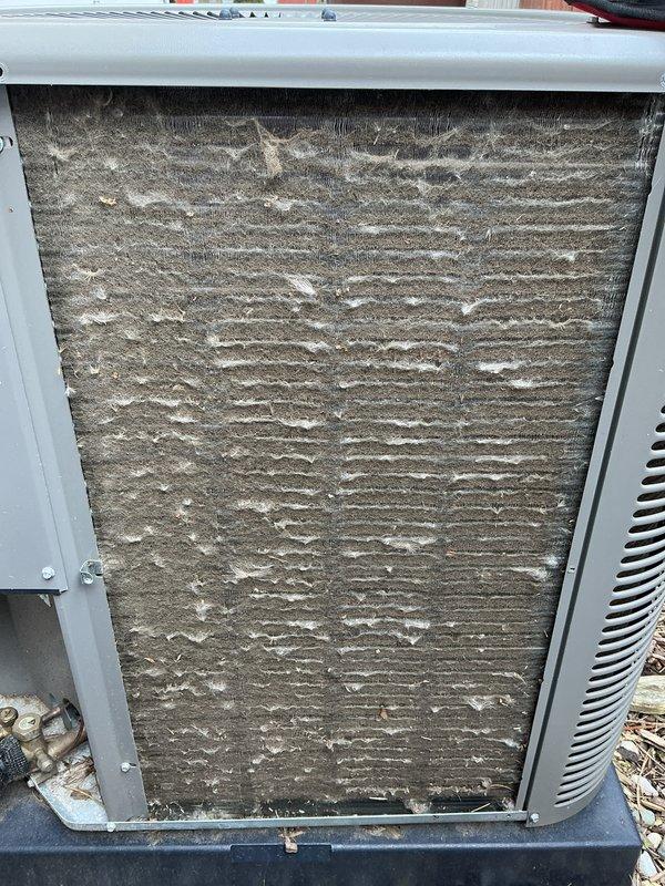 Completed ACM5/12-5 renewal maintenance on residential air conditioning unit located in side yard. Upon arrival, discovered heavily clogged air filter with excessive accumulation of dirt, dust, and debris throughout entire surface, significantly restricting airflow and reducing system efficiency. Removed and replaced contaminated filter with new unit per manufacturer specifications. Inspected outdoor condensing unit and surrounding area, noting wet ground conditions and proper drainage around equipment pad. Verified unit operation, airflow improvement, and proper system function following filter replacement. Documented equipment condition with photographs for service records.