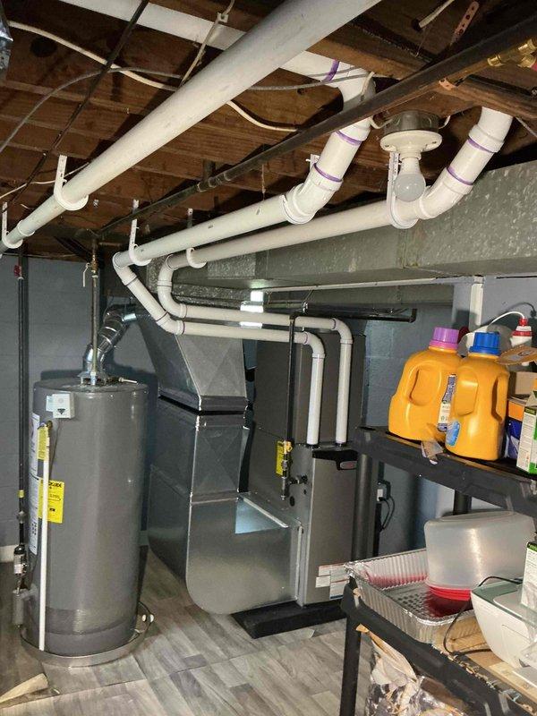 Completed full HVAC system installation including a 70,000 BTU furnace and 2.5-ton air conditioning unit. Installed new furnace in basement utility area with proper venting and condensate drainage using white PVC piping, integrated with existing ductwork system. Positioned outdoor condensing unit on rubber isolation pad at rear of property against exterior wall with pale yellow siding. Ran refrigerant lines and electrical connections from indoor air handler to outdoor unit using proper conduit and line set routing along exterior wall. Installed new dedicated electrical circuit to power system per code requirements. Secured all necessary mechanical and electrical permits prior to installation. Connected condensate drain lines with proper P-trap configuration and routed to exterior discharge point. Verified all electrical connections at outdoor disconnect and meter location. Tested system startup, confirmed proper refrigerant charge, airflow, and temperature differential across evaporato
