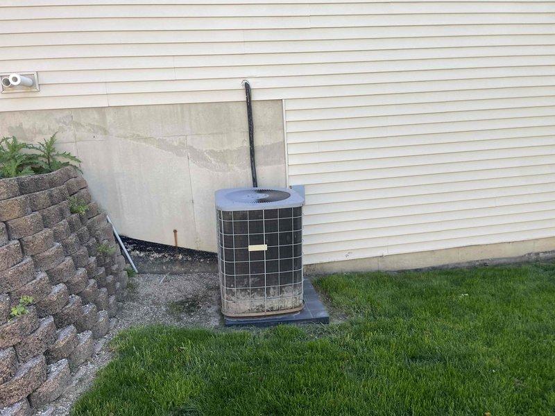 Conducted full system assessment of 16-year-old furnace and air conditioning unit to provide replacement estimates. Inspected outdoor condensing unit positioned on concrete pad with protective mesh cage, evaluated refrigerant line connections, electrical conduit routing, and overall system condition. Photographed equipment installation including exterior AC unit, electrical junction box, and conduit runs to document existing configuration for furnace-only replacement quote and complete HVAC system replacement quote as requested.