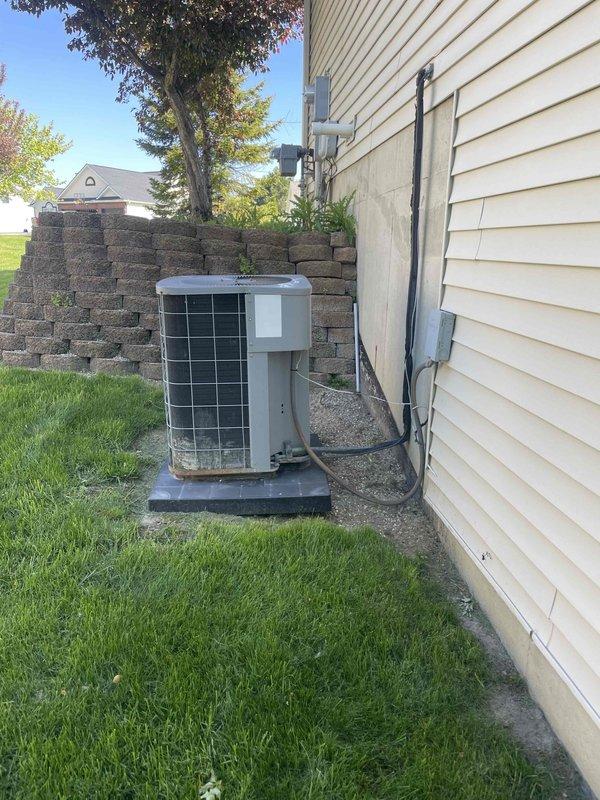 Conducted full system assessment of 16-year-old furnace and air conditioning unit to provide replacement estimates. Inspected outdoor condensing unit positioned on concrete pad with protective mesh cage, evaluated refrigerant line connections, electrical conduit routing, and overall system condition. Photographed equipment installation including exterior AC unit, electrical junction box, and conduit runs to document existing configuration for furnace-only replacement quote and complete HVAC system replacement quote as requested.