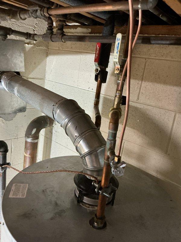 Responded to no hot water complaint at 55-year-old residential property. Upon inspection, diagnosed failed tanked water heater with suspected sediment accumulation affecting heating element performance. Assessed existing gas-fired water heater installation in basement utility area, including exhaust flue system with multiple elbows, copper supply lines with isolation valves (red and white handled ball valves), and associated piping infrastructure. Verified complete loss of hot water throughout home. Documented existing equipment condition and plumbing configuration via photographs showing flexible ductwork in attic/crawlspace area and basement mechanical room with water heater, flue pipe, and shut-off valve assembly. Provided assessment and recommendations for water heater repair or replacement options to restore hot water service.