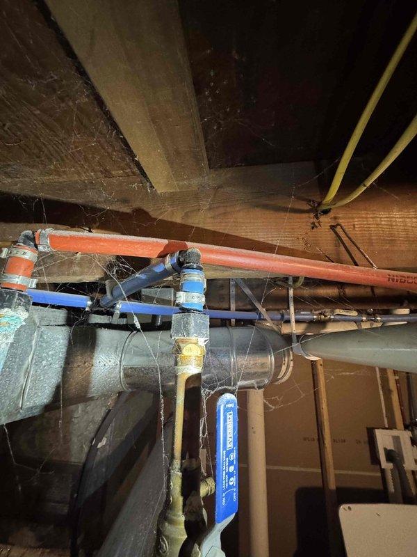 Responded to service call for reported leak and low water temperature issues at tankless water heater installation. Upon inspection, identified water accumulation in utility area beneath plumbing system. Examined tankless water heater connections, supply lines, and associated piping including copper supply lines, PEX distribution pipes, and isolation valves. Assessed all visible connections, fittings, and valve assemblies for signs of active leakage or seepage. Documented existing plumbing configuration including main supply connections with blue-handled isolation valves, branch piping, and ductwork proximity to water lines. Photographed installation for service records showing overhead utility space layout and mechanical equipment arrangement.