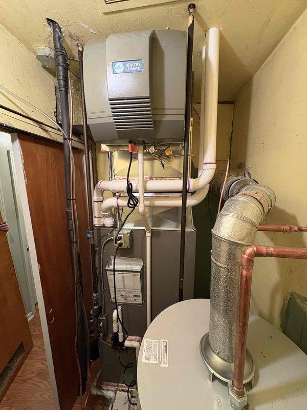 Completed full HVAC system installation in residential utility closet including 70,000 BTU gas furnace, 2-ton rear-discharge air conditioning unit, hot water heater, and whole-home humidifier. Installed and secured all equipment in confined space with proper clearances, ran and connected copper refrigerant lines, installed PVC condensate drainage system, and routed flexible ductwork for air distribution. Mounted Healthy Climate humidifier to supply plenum, installed water supply lines with proper insulation, and completed all electrical connections. Secured equipment with appropriate mounting brackets and metal strapping, reconnected existing utilities, and verified proper operation of all installed systems.