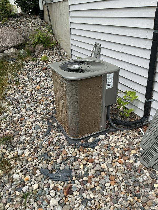 Completed annual cooling maintenance on residential split-system air conditioning condenser unit. Inspected outdoor unit positioned on landscaping rock bed against building exterior, noting heavily clogged condenser coils with significant dust, dirt, and debris accumulation blocking heat exchange surfaces. Cleaned condenser fins to restore proper airflow and system efficiency, removed organic debris from unit base, and verified refrigerant line connections and overall equipment operation per manufacturer specifications.
