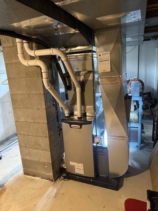 Completed installation of Lennox 70,000 BTU furnace in basement mechanical room. Unit mounted on platform with PVC venting routed overhead and connected to existing ductwork. All mechanical connections completed and system reconnected to operational status.