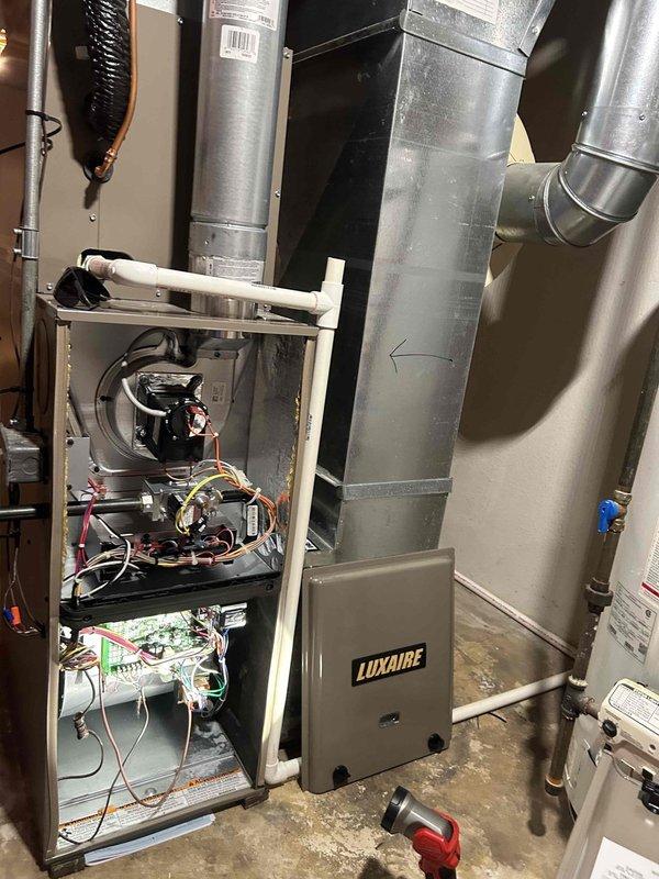 Responded to no cooling complaint on 8-year-old residential AC system. Upon arrival, inspected outdoor condenser units and indoor Luxaire furnace/air handler with access panel opened for diagnostic evaluation. Performed system assessment including electrical connections at disconnect box, refrigerant lines, and internal components. Documented equipment condition and configuration with photographic evidence showing dual outdoor units, ductwork, control boards, and wiring harness for service records.