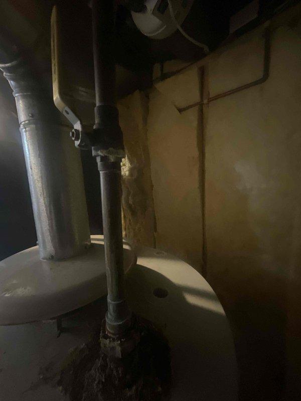 Conducted on-site evaluation of existing 15-year-old 75-gallon gas-fired water heater for replacement estimate. Inspected unit in basement mechanical room, documenting current condition including rust staining on tank top surface and corrosion present on adjacent piping at floor level. Assessed venting system configuration with existing metallic flue pipe connection and evaluated surrounding plumbing infrastructure including exposed copper lines and drainage systems. Photographed installation area to document spatial constraints, clearances, and existing utility connections for replacement specifications. Verified gas supply routing and evaluated ventilation requirements for new unit installation.