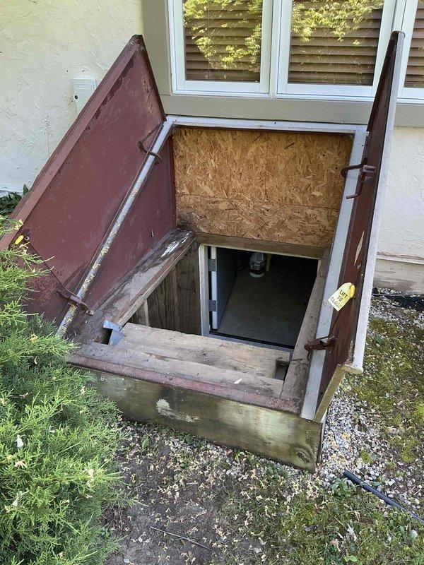 Conducted comprehensive site evaluation for replacement of 19-20 year old non-operational natural gas furnace and air conditioning system located in crawlspace. Assessed existing HVAC equipment accessed through exterior basement entry with weathered wooden frame and metal access doors. Documented current air handler unit with reflective foil wrap, flexible ductwork connections, and electrical wiring configuration in confined crawlspace environment. Evaluated structural conditions including exposed insulation, wooden framing, and equipment placement constraints. Provided detailed replacement estimate for complete furnace and A/C system upgrade to restore climate control functionality.