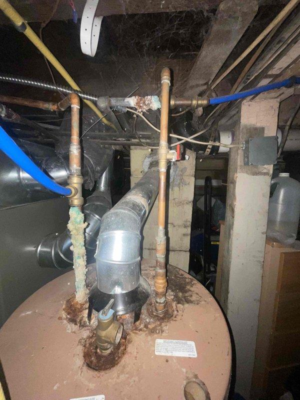 Conducted on-site evaluation of existing gas water heater in basement utility area. Upon inspection, unit displayed significant aging and deterioration including rust accumulation on tank top, heavy mineral deposits and corrosion on copper supply lines, and evidence of hard water scaling. Multiple copper pipes extending from tank top showed varying degrees of oxidation with white calcium buildup indicating potential past leaks or seepage. Water heater exhibited end-of-service-life conditions requiring full replacement. Documented equipment condition and surrounding installation area with photographs showing confined basement space with limited clearance, existing gas and water connections, and current venting configuration. Prepared comprehensive replacement estimate for new gas-fired water heater installation including removal and disposal of existing unit.