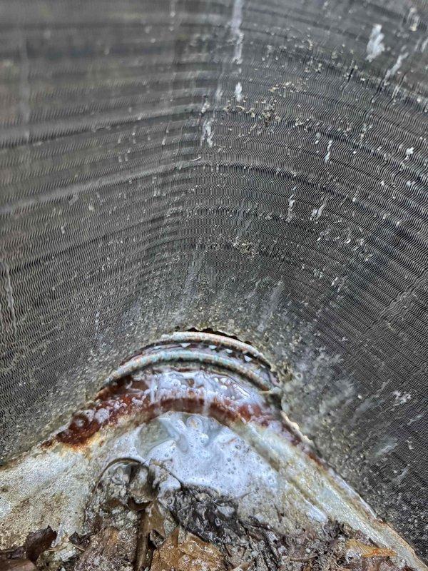 Responded to service call for AC unit not cooling properly on a two-year-old system. Upon inspection, discovered severely corroded copper refrigerant line with heavy oxidation and mineral deposits inside the ductwork, along with excessive moisture accumulation on interior duct surfaces. The corrosion indicates a refrigerant leak that has been ongoing, which explains the reduced cooling capacity. Documented the corroded line and moisture conditions with photos for record. Advised that the refrigerant line requires replacement and system will need proper refrigerant charge after repair is completed. Unit exterior shows normal wear for outdoor installation on rock bed foundation.
