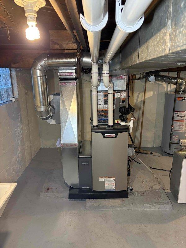 Completed full HVAC system installation in basement utility area, including 70,000 BTU furnace with exposed control panel and circuit board section, 2-ton air conditioning unit with rear placement configuration, and humidifier integration. Installed white PVC venting system extending from furnace to ceiling with proper exhaust routing, connected silver metallic supply and return ductwork with vertical-to-horizontal elbow transitions, and established all electrical connections with black cabling routed along ceiling joists. Reconnected existing utilities and verified proper operation of all mechanical systems. All equipment positioned on concrete floor with adequate clearance for service access, permits obtained prior to installation, and system tested for proper airflow and functionality.