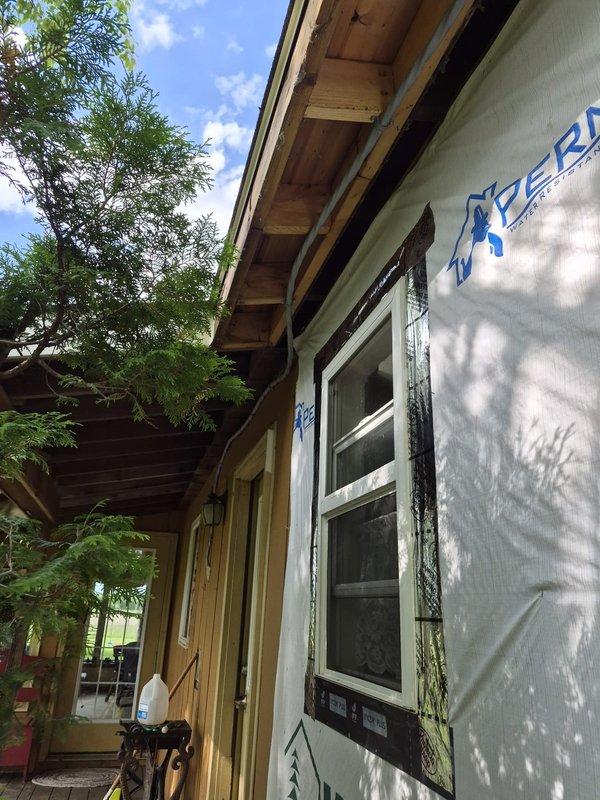 Conducted site consultation with carpenter to assess exterior siding removal requirements for upcoming electrical work. Documented current construction phase showing house wrap installation, window weatherproofing, and exposed framing, and inspected existing electrical panel configuration with labeled circuit breakers to determine integration points for planned fixture and outlet installations.