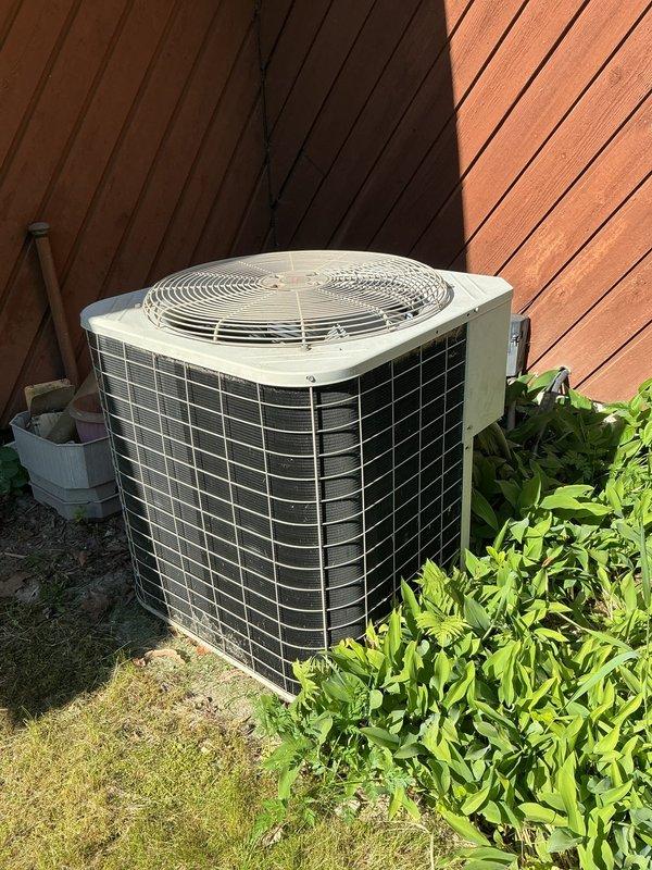 Responded to service call for 20+ year old outdoor air conditioning unit with suspected refrigerant leak in coil. Upon arrival, performed visual inspection of condenser unit positioned against building exterior. Noted unit showing significant age-related wear with dirty condenser coils containing accumulated debris, cobwebs, and fibrous material between fins. Information plate on unit panel heavily weathered with faded specifications. Assessed system for refrigerant leak as reported, examining evaporator coil condition and checking for signs of refrigerant loss. Unit requires thorough coil cleaning to restore proper airflow and heat transfer efficiency before further diagnostics can determine extent of refrigerant system issues.