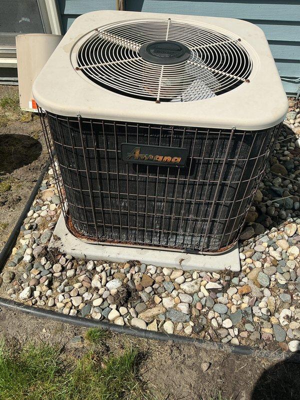 Completed comprehensive air conditioning maintenance on 19-year-old Amana condensing unit and Ruud Achiever 90 Plus furnace system under membership agreement. Performed full AC tune-up including inspection of outdoor condensing unit showing age-related weathering and rust staining on lower cabinet and grille sections, verified refrigerant levels, cleaned condenser coils, checked electrical connections and capacitor operation, and inspected fan motor assembly. Evaluated indoor air handler components, examined ductwork connections for proper sealing, verified condensate drain lines and PVC drainage system for proper flow, tested thermostat operation and system cycling. Confirmed system operational at conclusion of maintenance with all components functioning within normal parameters despite advanced age of equipment. Documented equipment condition with photographs showing outdoor unit on concrete pad with river rock landscaping and indoor mechanical room installation. System ready for coo