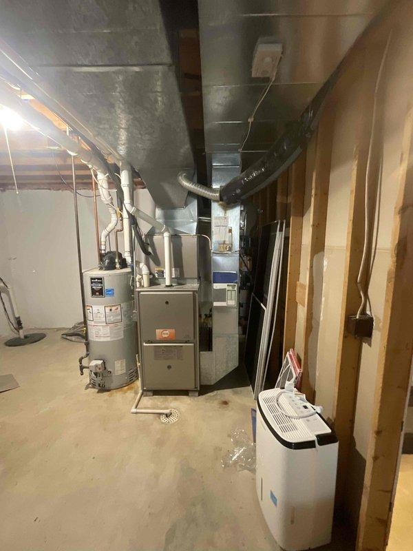 Responded to service call for non-operational air conditioning system affecting entire residence with 15-year-old HVAC equipment. Assessed existing basement mechanical room containing aging furnace, water heater, and associated ductwork infrastructure. Provided comprehensive estimate for furnace-only replacement, documenting current system configuration including gray metal furnace unit, cylindrical water heater, silver metallic ductwork distribution, and PVC venting arrangements in unfinished basement utility space with concrete flooring and exposed framing.