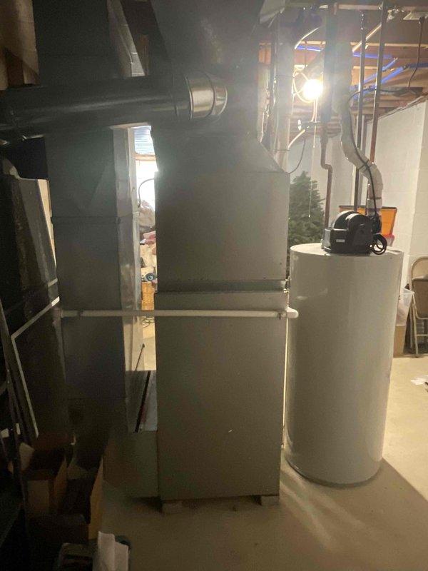 Responded to service call for non-operational air conditioning system affecting entire residence with 15-year-old HVAC equipment. Assessed existing basement mechanical room containing aging furnace, water heater, and associated ductwork infrastructure. Provided comprehensive estimate for furnace-only replacement, documenting current system configuration including gray metal furnace unit, cylindrical water heater, silver metallic ductwork distribution, and PVC venting arrangements in unfinished basement utility space with concrete flooring and exposed framing.