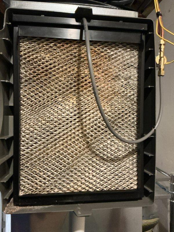 Completed annual cooling maintenance on residential HVAC system. Inspected outdoor condensing unit with cylindrical design, verified proper operation and clearance from surrounding vegetation and debris. Examined indoor air handler components including humidifier pad assembly, noting moderate dust accumulation and discoloration on mesh filter media. Checked refrigerant line connections and condensate drainage system. Unit operating within normal parameters with no immediate service concerns identified.