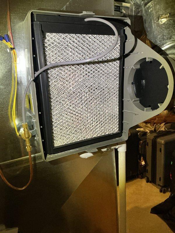 Completed annual cooling maintenance on residential HVAC system. Inspected indoor air handler unit and replaced furnace filter with new mesh filter panel installed in metal frame housing. Verified proper airflow through ductwork and connections. Proceeded to outdoor condensing unit for exterior inspection. Examined beige AC unit mounted on plastic pad against building foundation. Inspected fan grille, louvered vents, and refrigerant line connections. Verified electrical conduit routing and manufacturer specifications. Confirmed unit operating within normal parameters with no visible signs of damage or wear. All components functioning properly upon completion of maintenance service. Wore shoe covers per customer request throughout interior portion of service call.