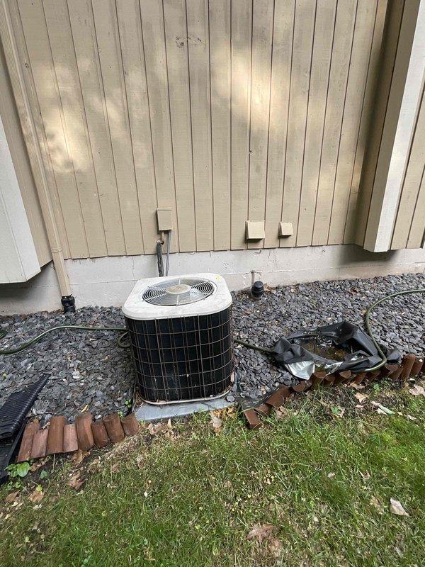 Conducted on-site assessment for complete HVAC system replacement estimate at approximately 1,900 sq ft single-family residence. Evaluated existing outdoor air conditioning condenser unit positioned on concrete pad with gravel surround against exterior wall, and basement-located gas furnace of unknown age. Documented current equipment configuration including electrical service, refrigerant line routing, and duct transitions. Photographed existing condenser installation showing white cabinet unit with protective top grille, electrical conduit and disconnect box mounting, and surrounding site conditions. Prepared comprehensive replacement quote for cost-effective system including new air conditioning unit and gas furnace, complete removal and disposal of existing equipment, installation of standard refrigerant line set, duct transition work, permit acquisition and inspection coordination, basic thermostat provision if required, and full warranty coverage details.