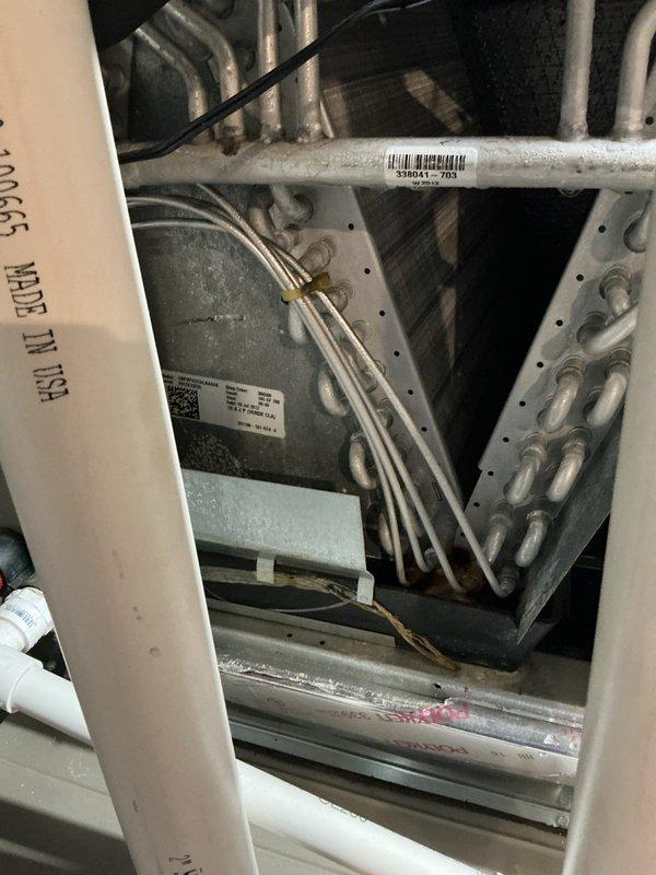 Performed comprehensive seasonal air conditioning maintenance on a five-year-old system with no reported cooling issues. Conducted complete system inspection including examination of refrigerant lines, evaporator coil, blower assembly, and all accessible HVAC components. Inspected humidifier pad which showed typical mineral deposits and discoloration consistent with normal operation. Verified all copper refrigerant lines, brass fittings, and connections for proper condition and secure mounting. Checked condensate drainage system including PVC drain lines for proper flow and blockage prevention. Examined blower motor housing and fan assembly for proper operation. Inspected all electrical connections, wiring, and control components within the unit. Verified system labeling and technical specifications on equipment panels. Documented system condition through photographic records of internal components including evaporator section, refrigerant piping with barcode identification, and humidi