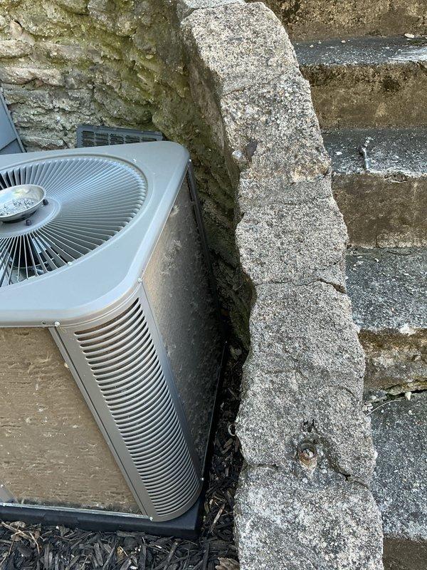Completed annual cooling maintenance on outdoor condensing unit. Inspected unit exterior, refrigerant lines, and electrical connections. Noted significant dirt and debris accumulation on condenser coils requiring cleaning. Unit positioned on mulch bed against stone exterior wall with evidence of moisture and organic growth on surrounding building materials. Documented equipment condition with photographs showing heavily soiled filter panel with vertical streaking and discoloration patterns indicating restricted airflow. Verified fan assembly and louvered vent panels. Unit operational following maintenance procedures.
