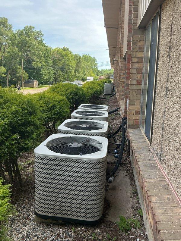 Responded to no cooling complaint for multiple Gibson-branded air conditioning units over 20 years old. Upon arrival, found four condenser units installed on concrete pad with gravel base against building exterior. Performed visual inspection of all units, checking refrigerant line connections, electrical conduits, and overall equipment condition. Documented existing equipment configuration showing two pairs of units with black refrigerant lines routed up brick wall and standard wire fan guards in place. Units exhibited age-appropriate wear consistent with 20+ year service life. Given the advanced age of the equipment and no cooling condition, advised customer that these systems have exceeded their typical 15-year lifespan and replacement would be more cost-effective than repair. Photographed installation for documentation purposes showing equipment layout, mounting configuration, and connection points. Customer provided contact information for follow-up consultation regarding replacem