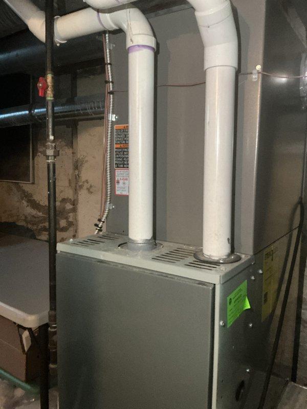 Completed routine Air Care Cooling maintenance inspection on residential HVAC system. Inspected gray two-tone furnace unit, verified all warning labels and specifications were properly affixed, and confirmed white PVC exhaust and intake venting connections were secure. Examined copper piping, metal ductwork connections, gas line with red valve handle, and flexible black ductwork for proper operation. All equipment found to be in normal operational condition with no service needs identified at this time.